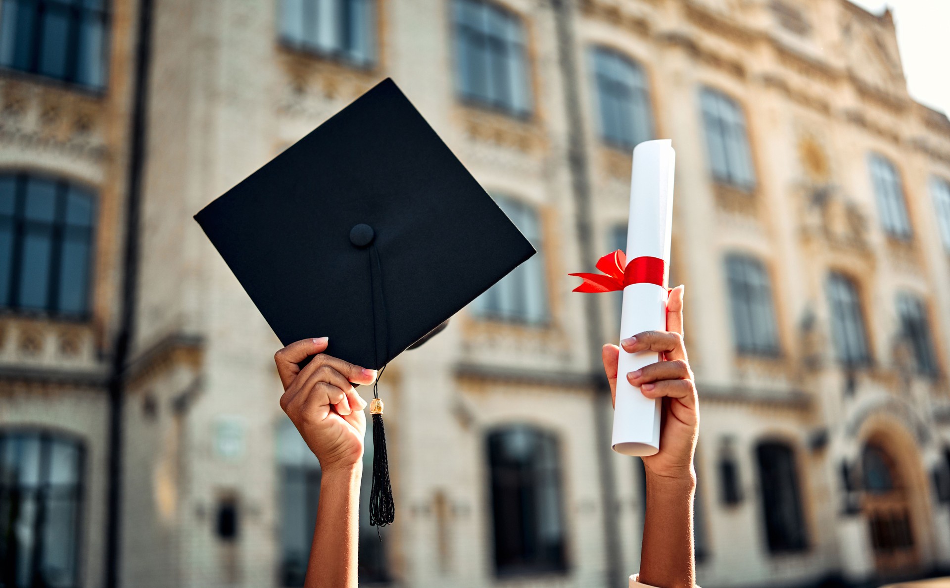 Cropped image of graduate holding academic hat and diploma with red ribbon. Happy graduation, bright future, success and confidence.